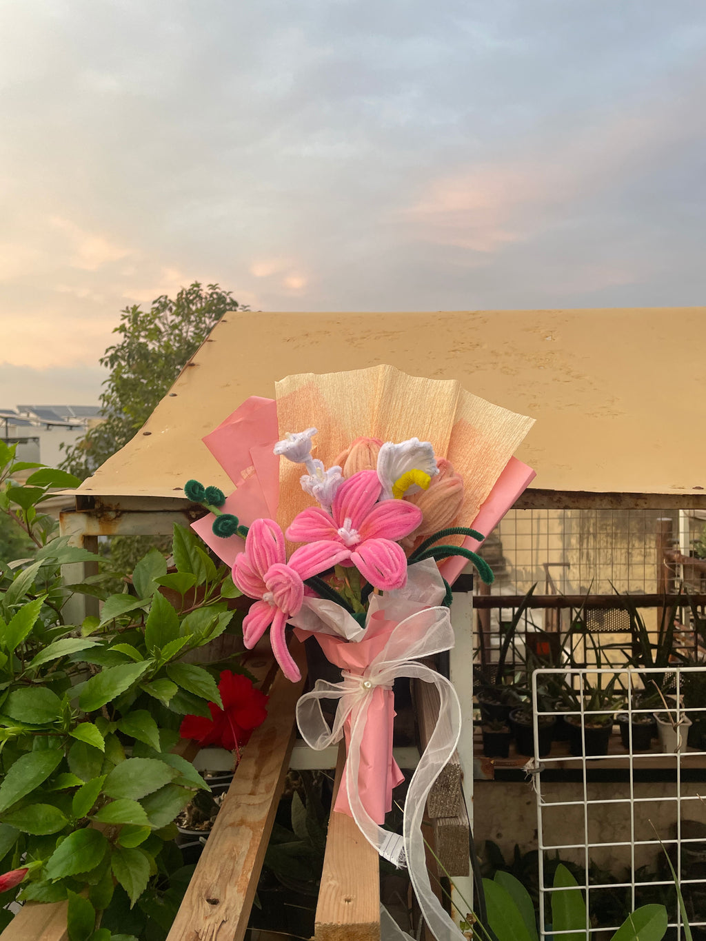 Decorative flower arrangement with pink flowers and a white bow in front of a building.