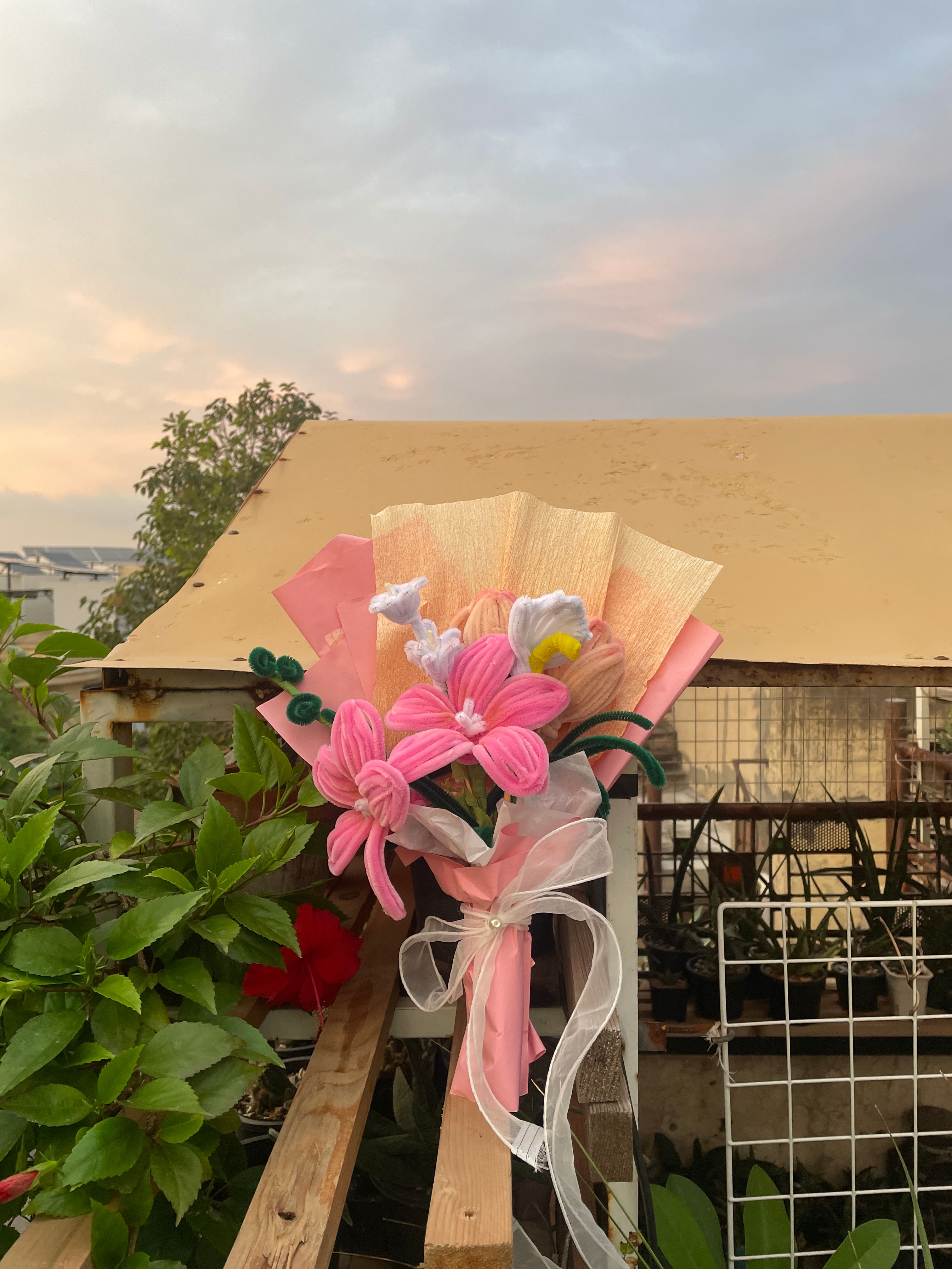 Decorative flower arrangement with pink flowers and a white bow in front of a building.