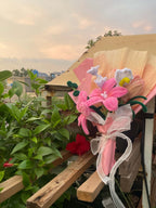 Bouquet of pink flowers with green leaves on a wooden deck with plants in the background