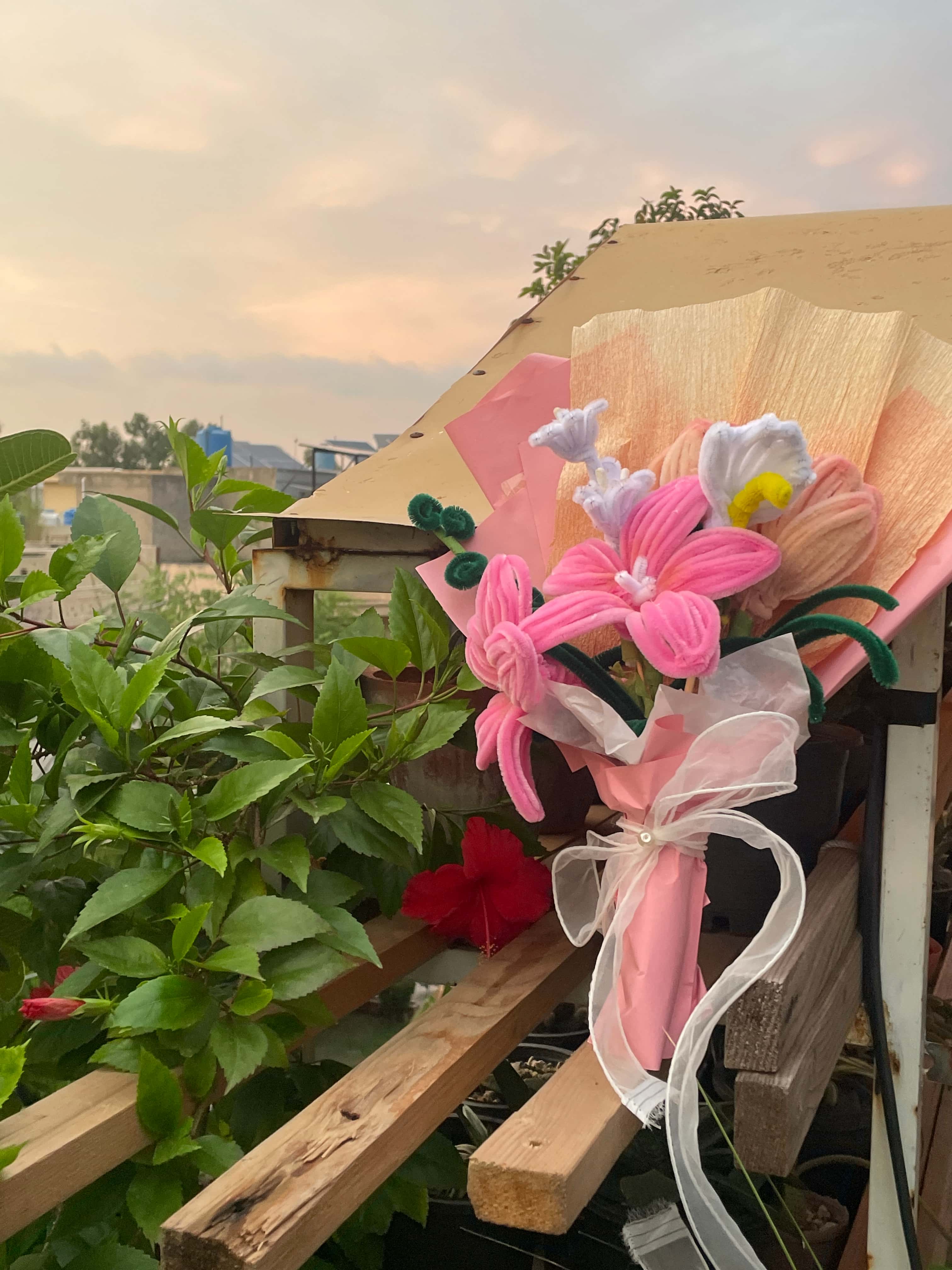 Bouquet of pink flowers with green leaves on a wooden deck with plants in the background