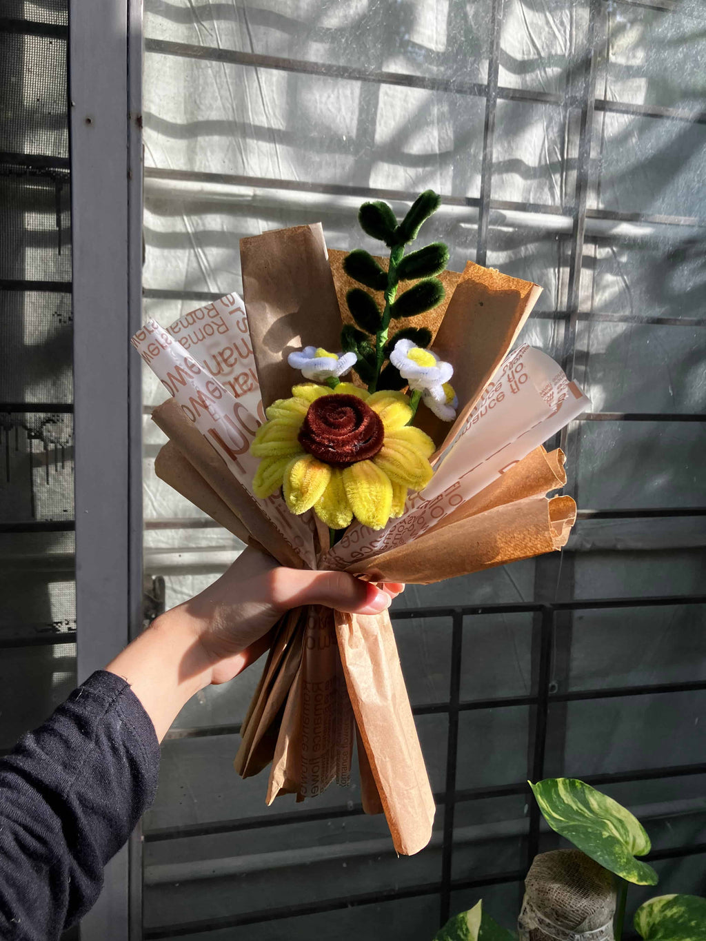 Hand holding a bouquet made of books and flowers against a window background