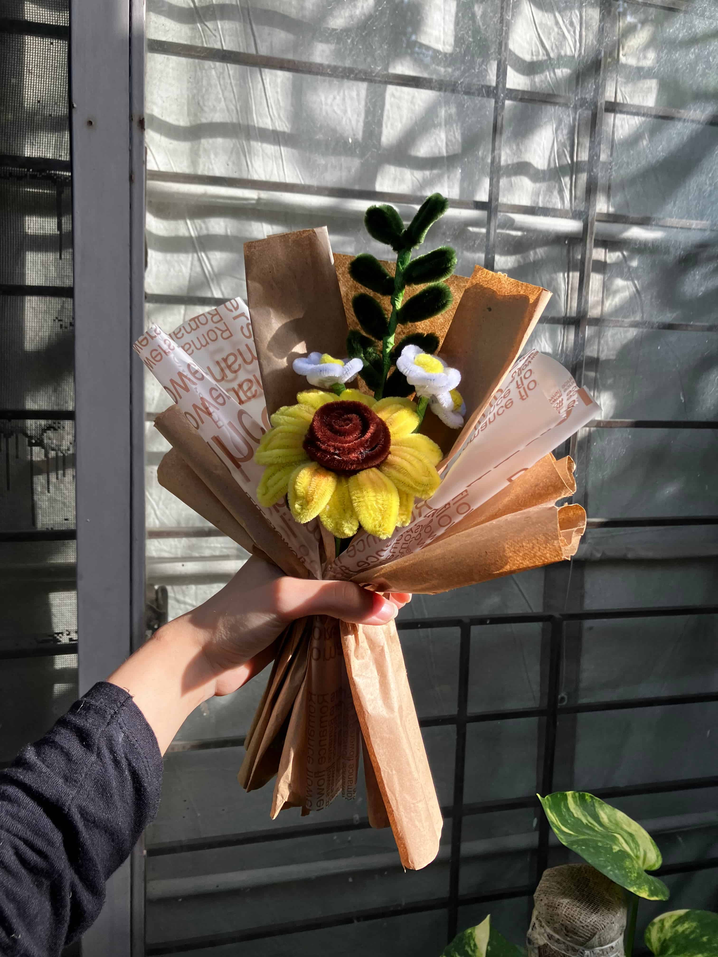 Hand holding a bouquet made of books and flowers against a window background