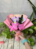 Bouquet of pink flowers with decorative ribbons held by a person on a wooden surface.