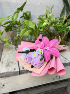 Bouquet of pink and purple artificial flowers on a wooden surface with plants in the background
