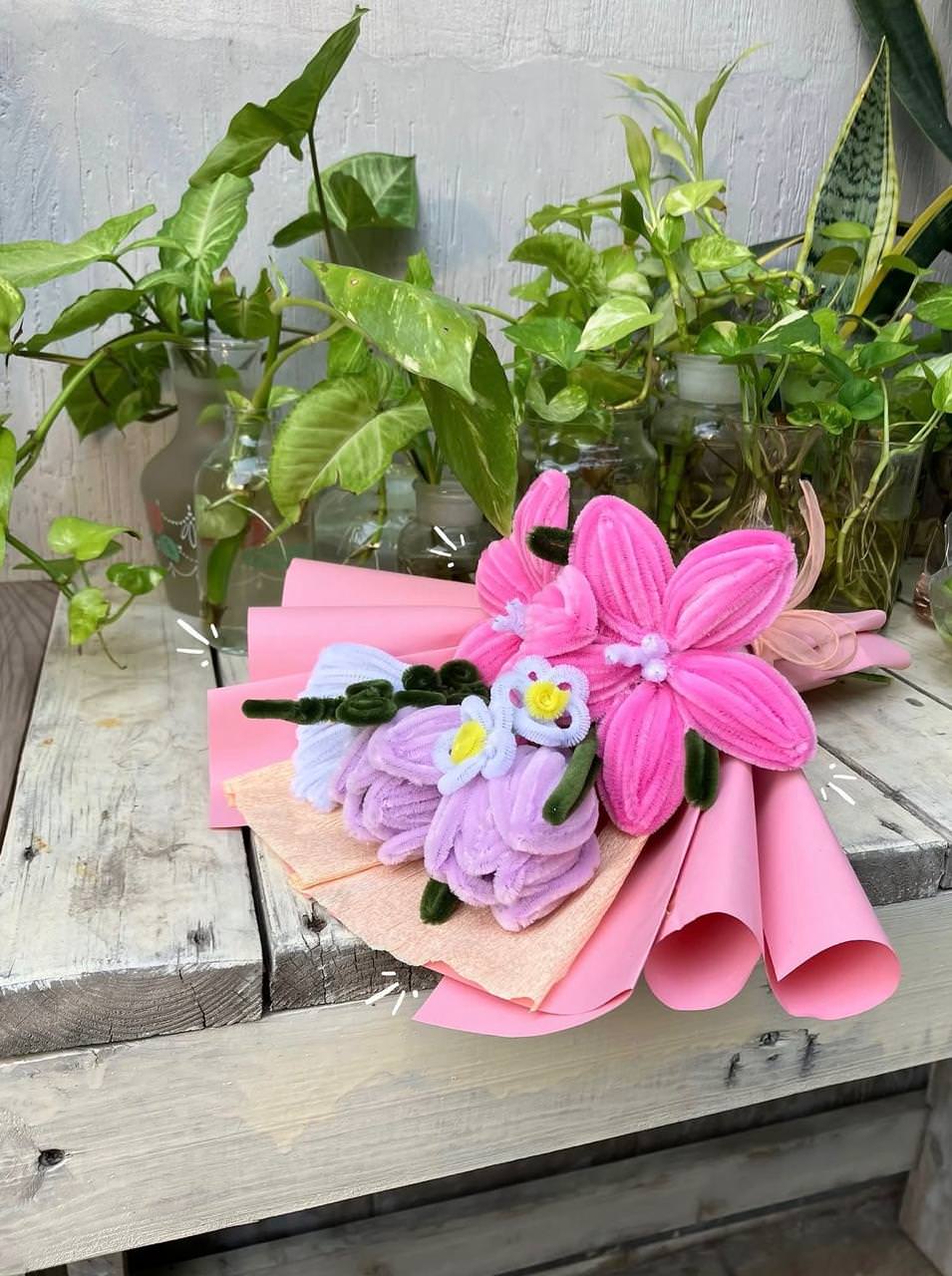 Bouquet of pink and purple artificial flowers on a wooden surface with plants in the background