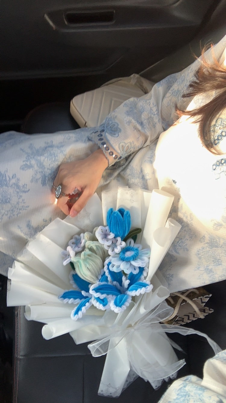Person holding a white fan with blue floral decorations inside a vehicle.