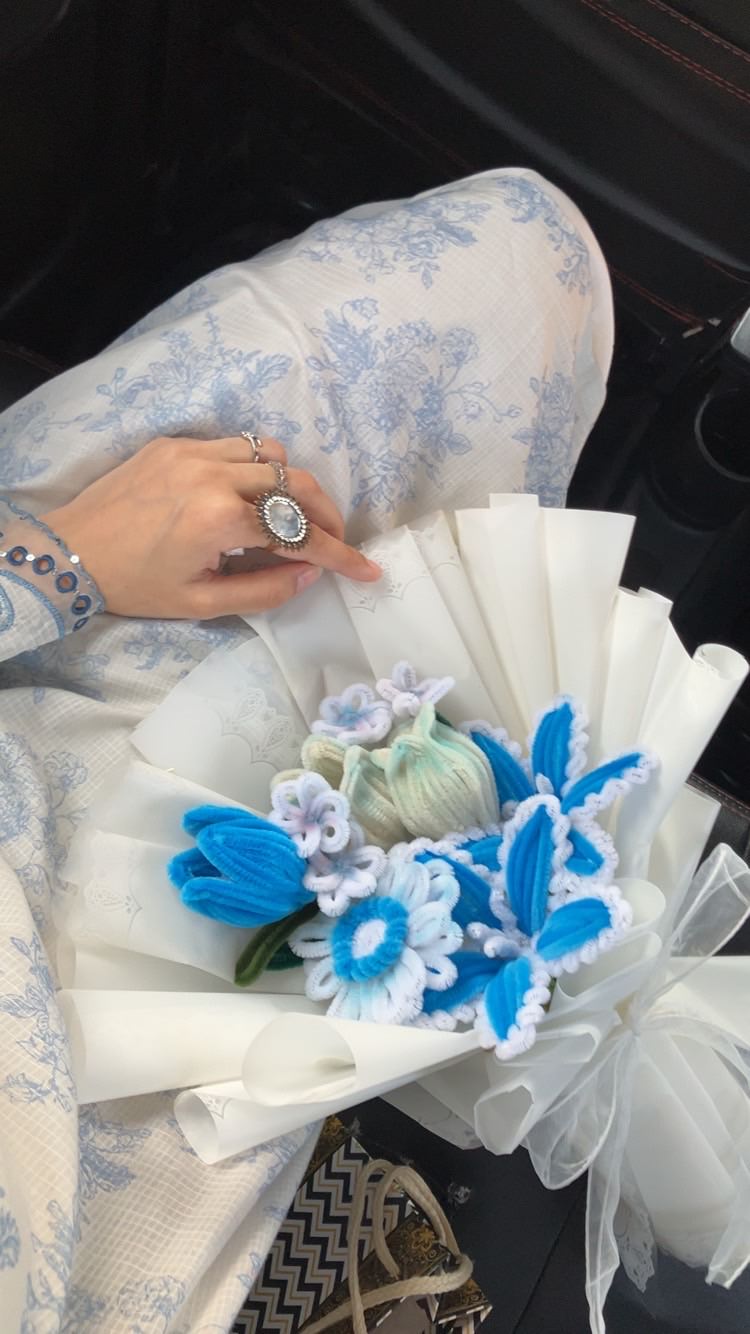 Bouquet of flowers with blue and white decorations held by a person wearing a ring.