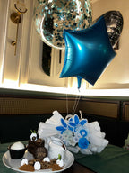 Decorative setup with blue balloon, flowers, and a cake on a table.
