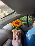 Hand holding a decorative sunflower in a cupcake holder inside a car.