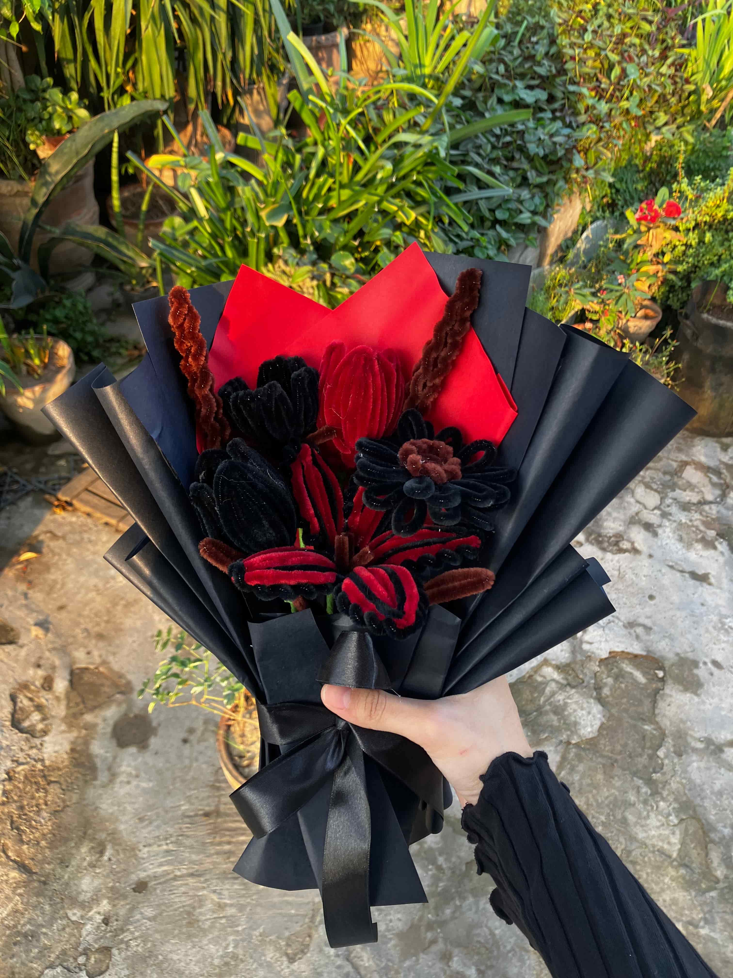 Bouquet of black and red flowers held by a person outdoors.