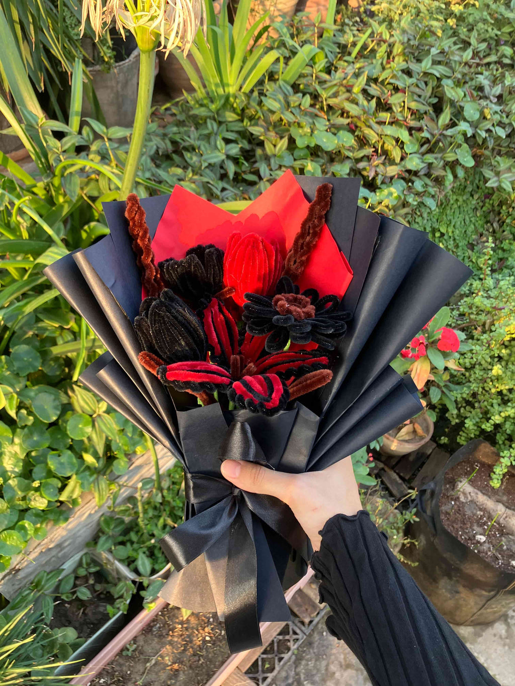 Bouquet of red and black flowers wrapped in black paper held by a person outdoors.