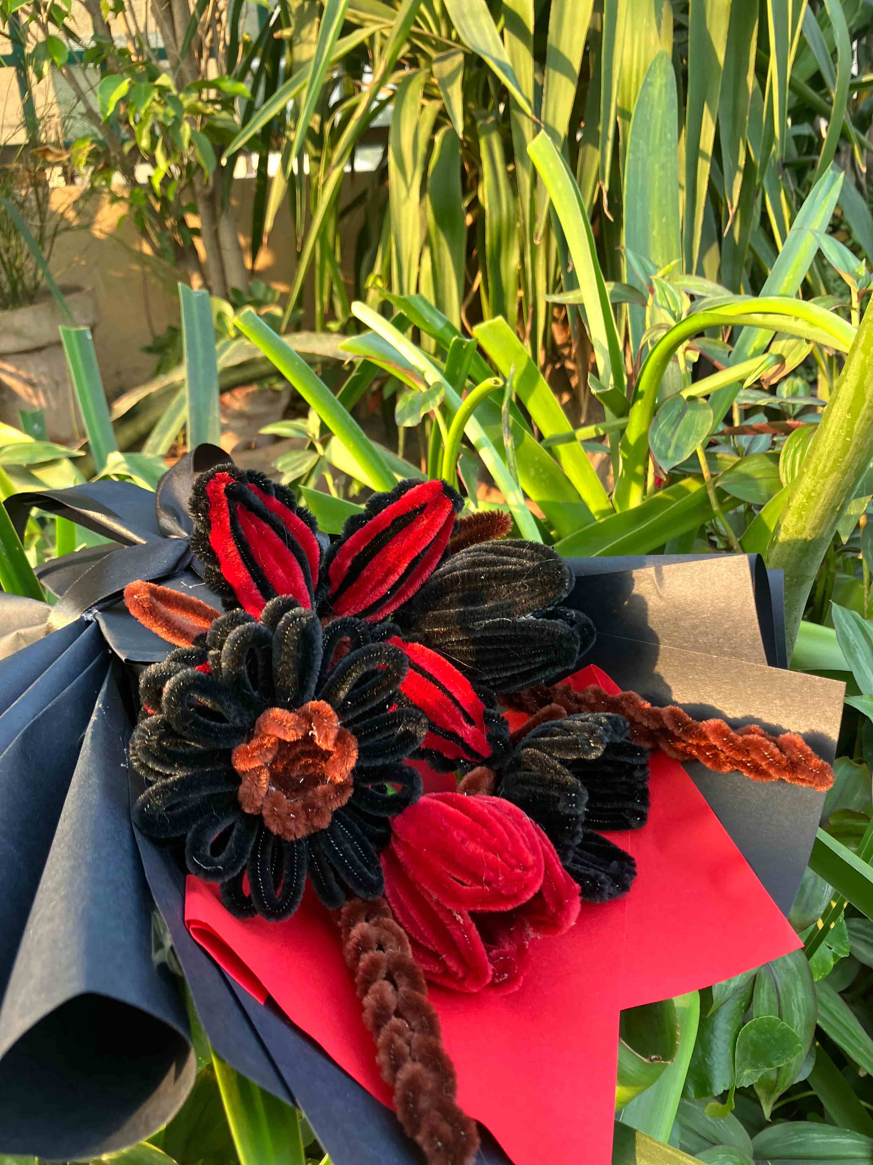 Colorful flower arrangement with red, black, and brown flowers on a green leafy background
