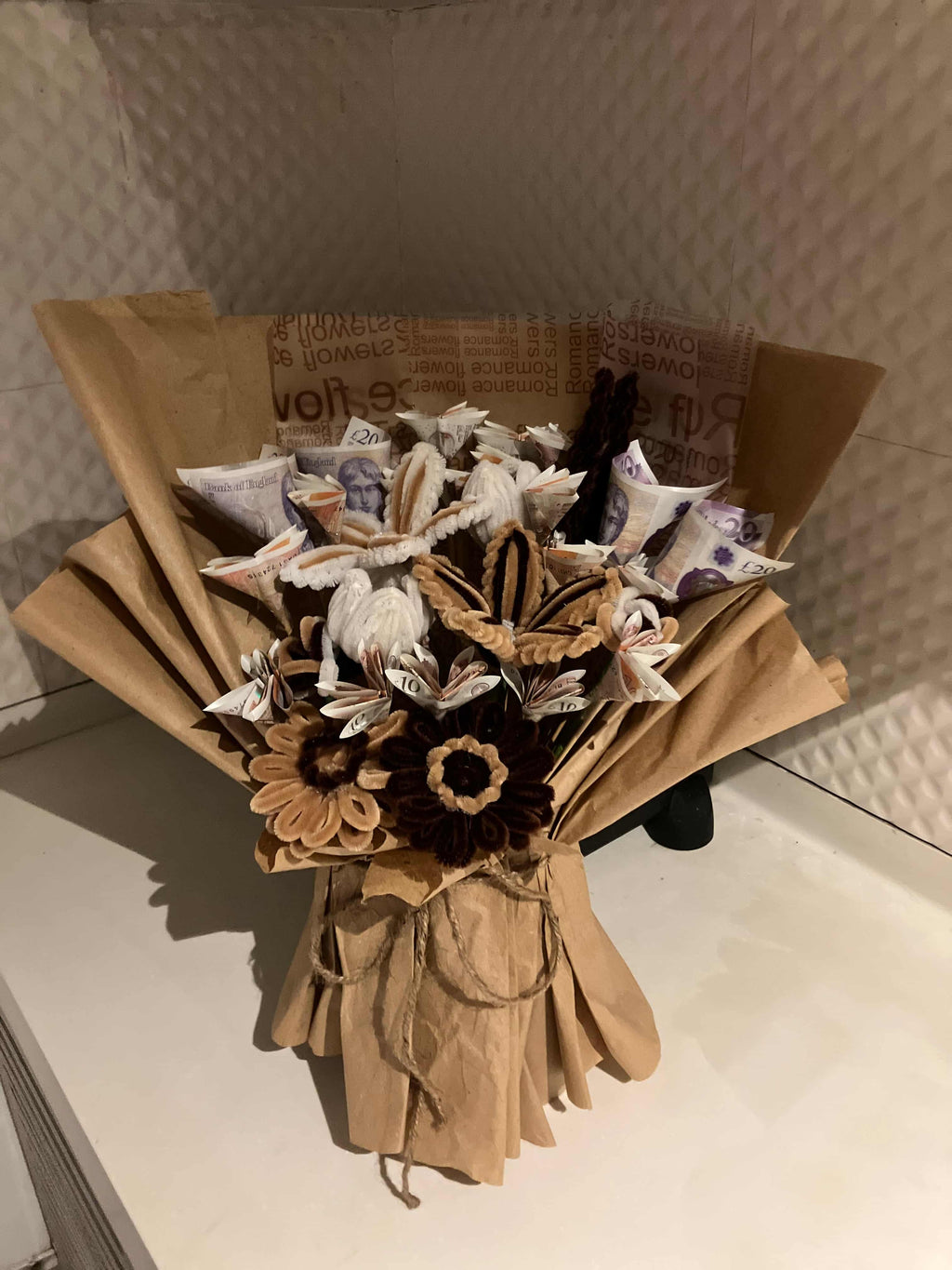 Bouquet of dried flowers and leaves in a cardboard box on a textured surface.