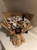 Bouquet of dried flowers and leaves in a cardboard box on a textured surface.