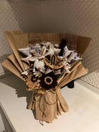 Bouquet of dried flowers and leaves in a cardboard box on a textured surface.