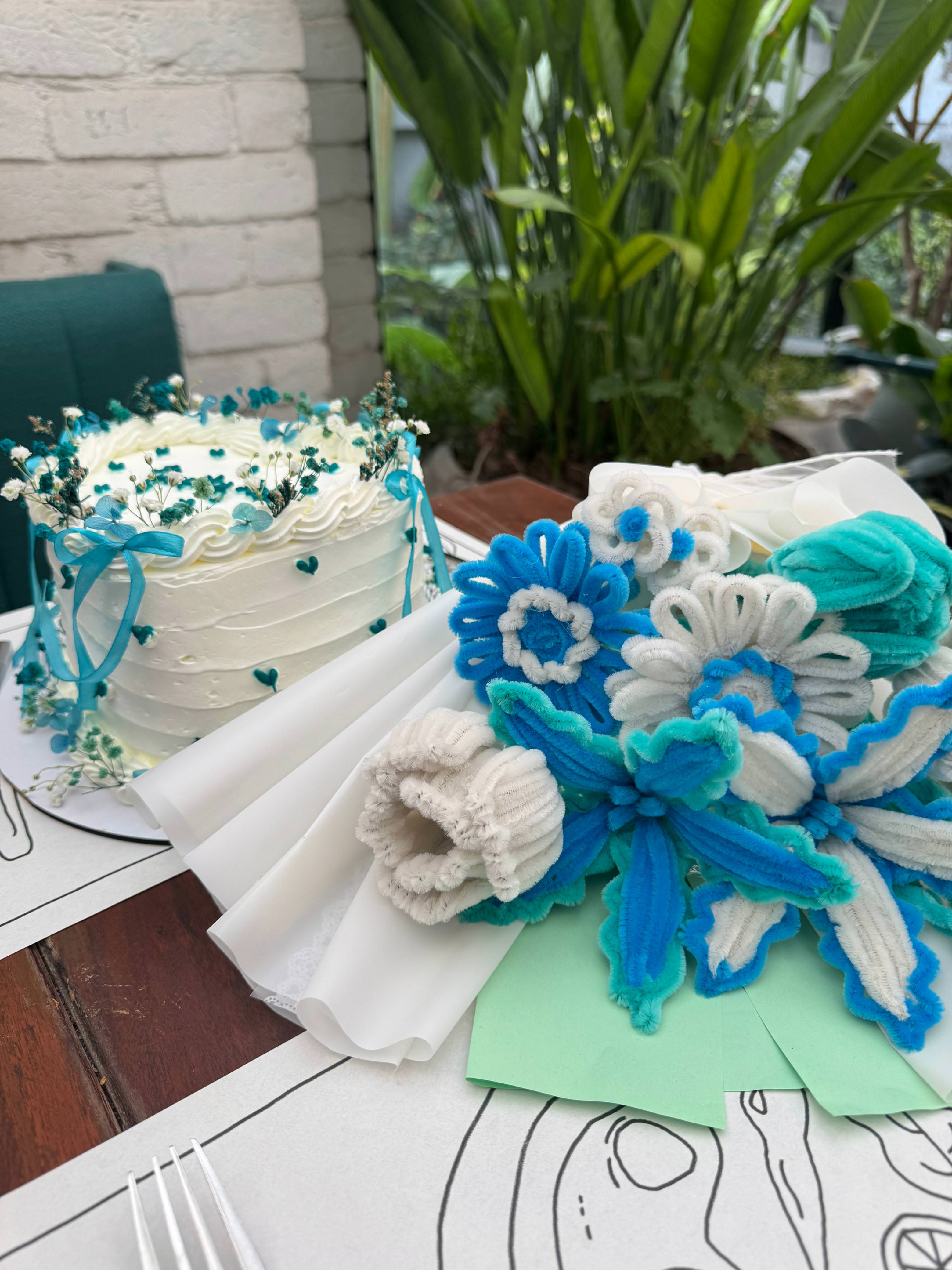 Decorative cake with blue and white flowers on a table outdoors.