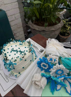 Decorative cake with blue and white flowers on a table with plants in the background