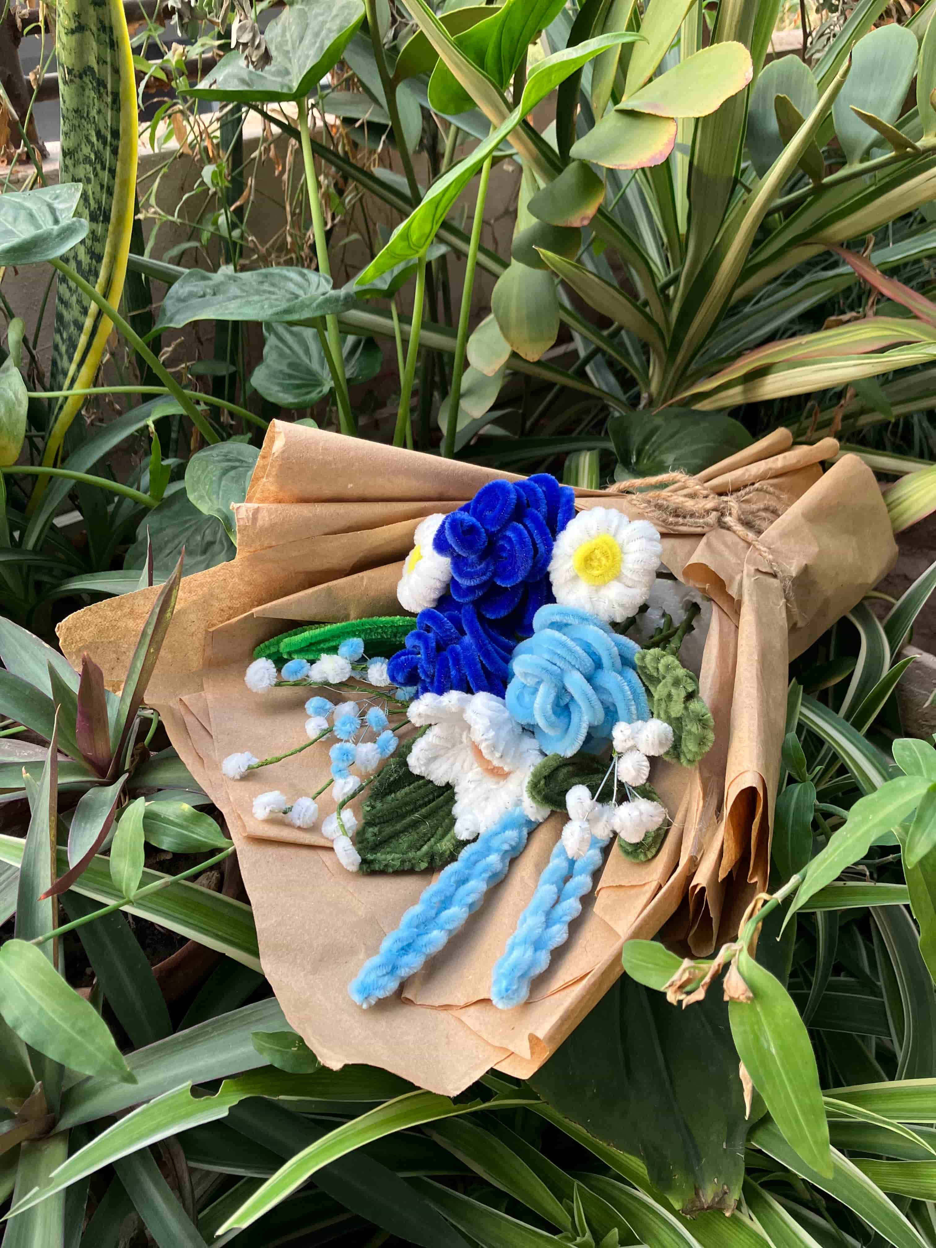 Bouquet of artificial flowers on a brown paper bag with green plants in the background