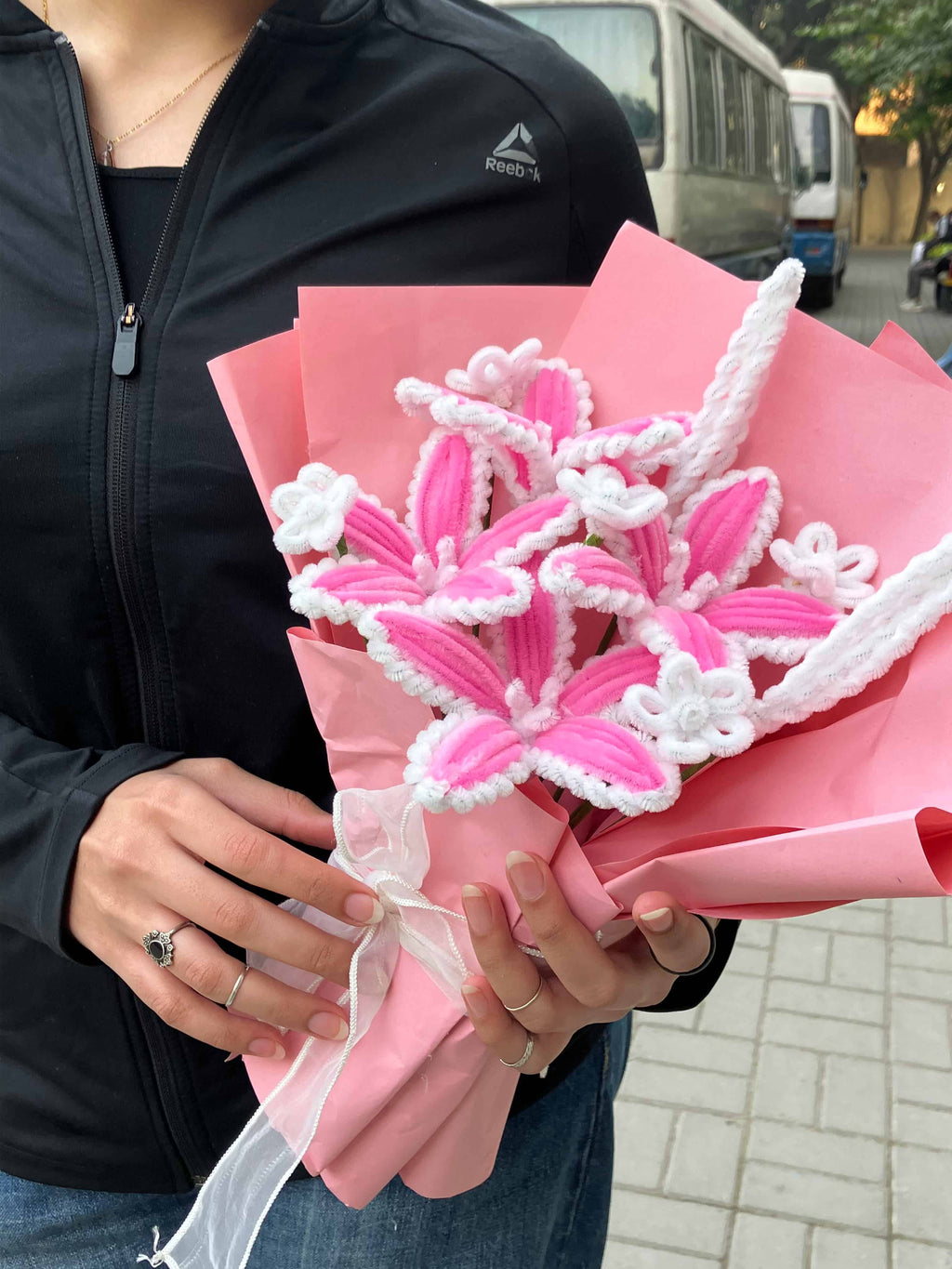 Person holding a pink and white decorative item, possibly a flower or ribbon, with a blurred background.