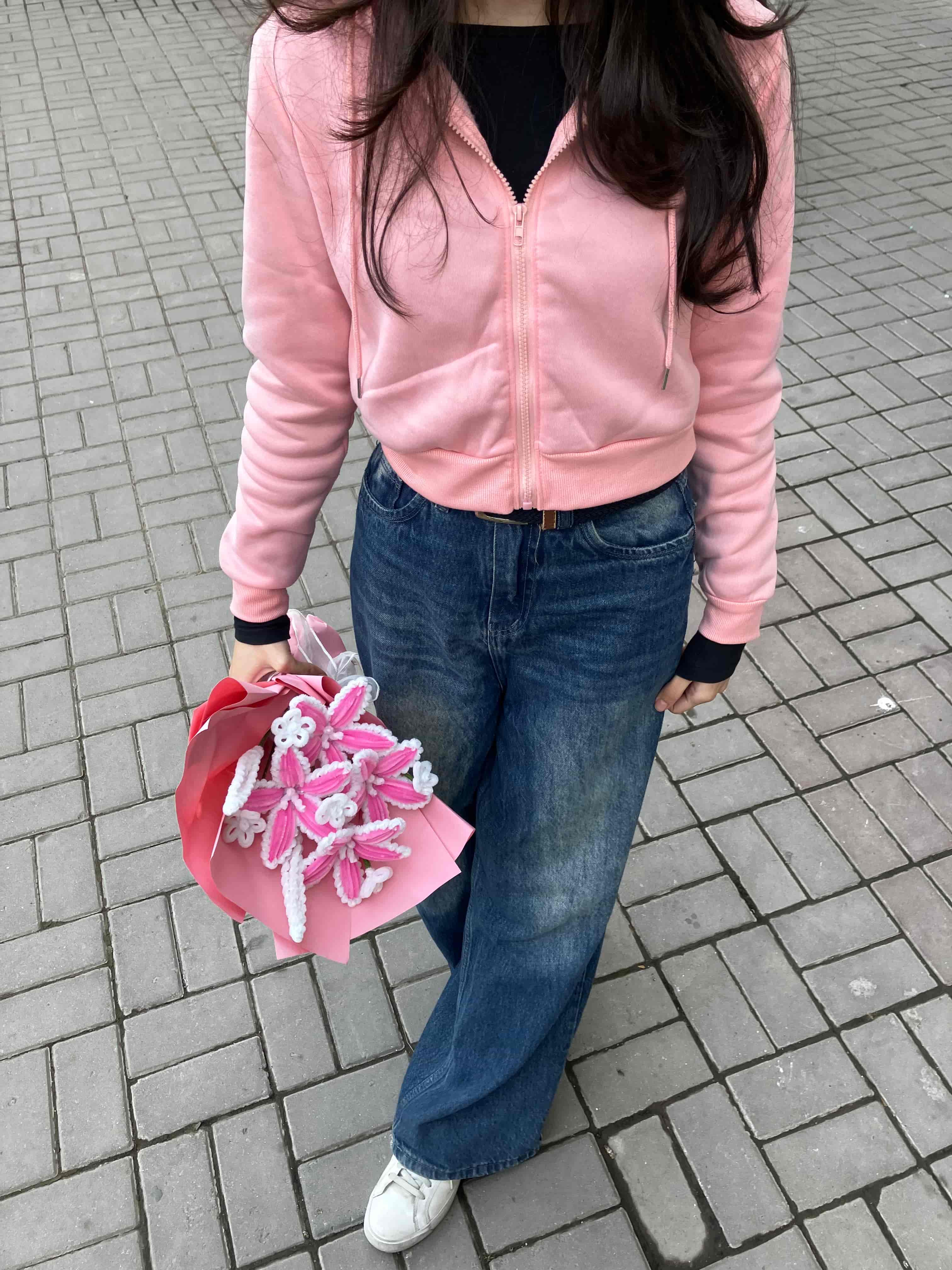 Person holding a pink flower arrangement on a tiled pavement