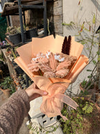 Bouquet of flowers wrapped in brown paper with a decorative bow, held outdoors.
