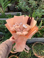 Bouquet of flowers wrapped in peach paper held by a person with plants in the background