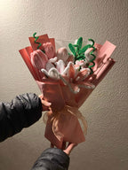 Bouquet of pink tulips wrapped in brown paper with a bow, held against a plain wall.