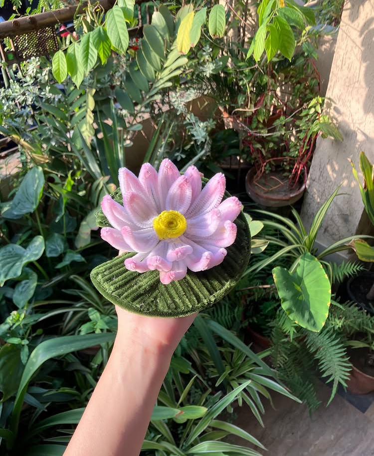 Pink artificial flower held by a hand among green plants