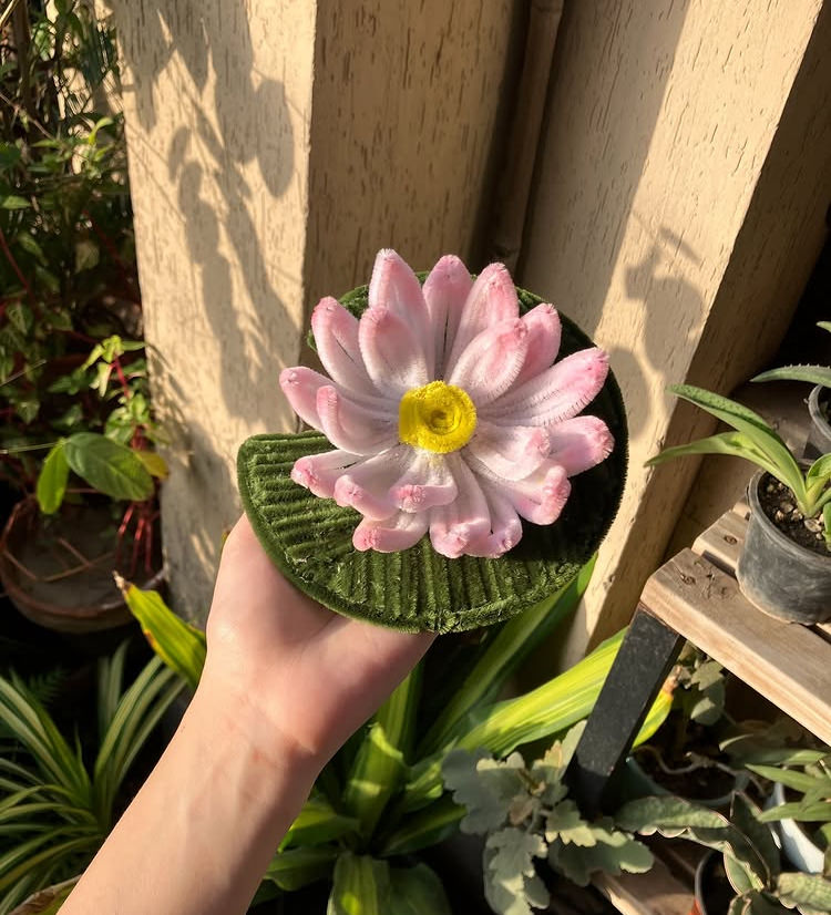 Hand holding a pink ceramic flower against a garden background