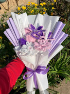 Bouquet of flowers with purple and white ribbons held by a person wearing a red sleeve.