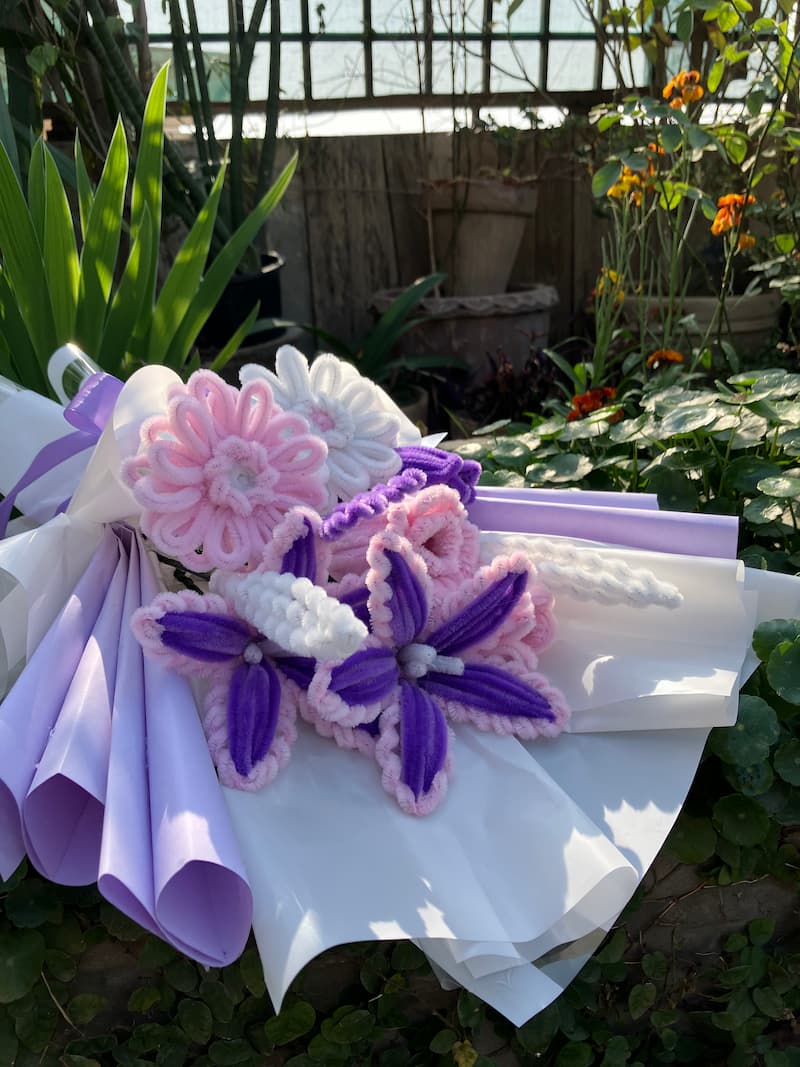 Decorative flower arrangement with purple and pink flowers on a white background, surrounded by greenery.