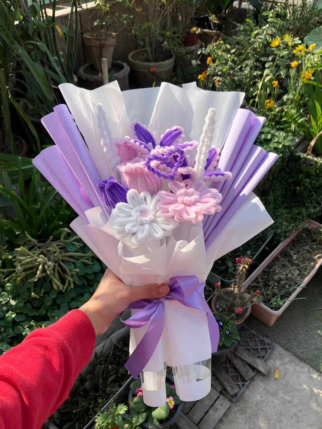 Bouquet of flowers with purple and white ribbons held by a person in a garden setting.
