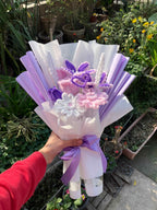 Bouquet of flowers with purple and white ribbons held by a person in a garden setting.