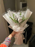 Bouquet of white tulips in a clear plastic wrap held by a person with a colorful sleeve.