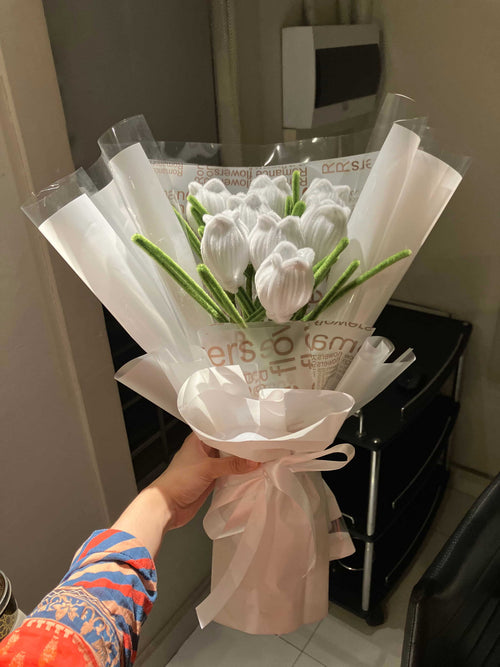 Bouquet of white tulips in a clear plastic wrap held by a person with a colorful sleeve.
