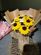 Bouquet of yellow and brown flowers wrapped in brown paper on a checkered tablecloth.