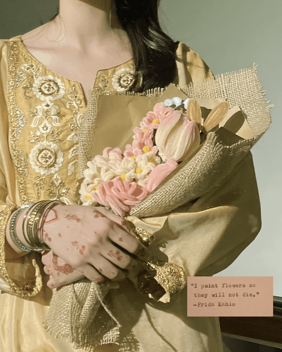 Person holding a bouquet of flowers wearing a gold embroidered outfit with a quote on a pink card.