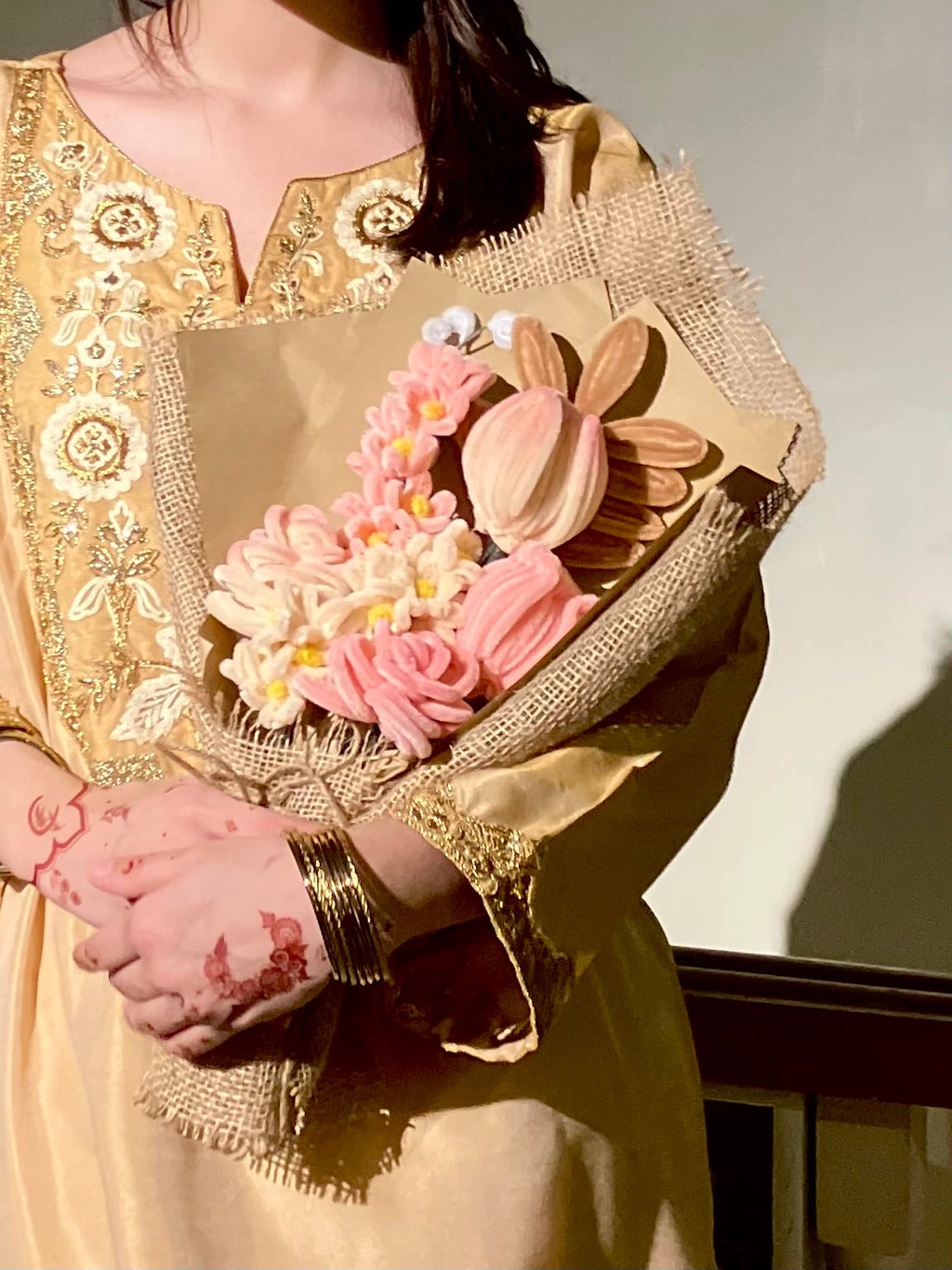 Person holding a bouquet of flowers wrapped in gold fabric against a neutral background