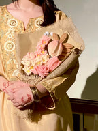 Person holding a bouquet of flowers wrapped in gold fabric against a neutral background