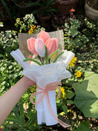 Bouquet of pink tulips with a white ribbon held by a hand against a green leafy background.