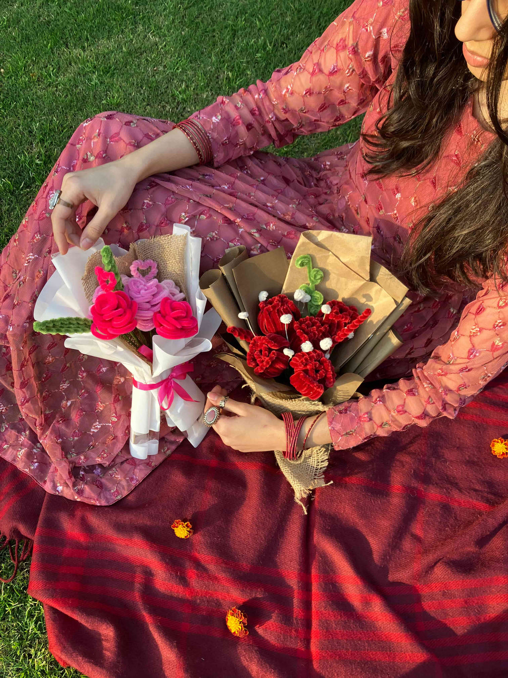 Two women sitting on grass holding flower bouquets.