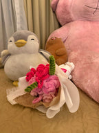 Plush toys including a penguin, bear, and pink flower arrangement on a bed.