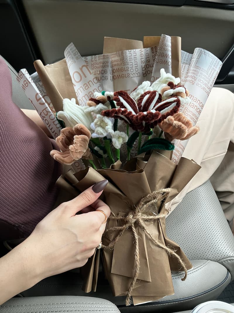 Hand arranging a decorative wreath with paper and fabric on a car seat.