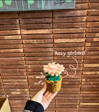 Hand holding a small decorative item with flowers against a wooden wall.