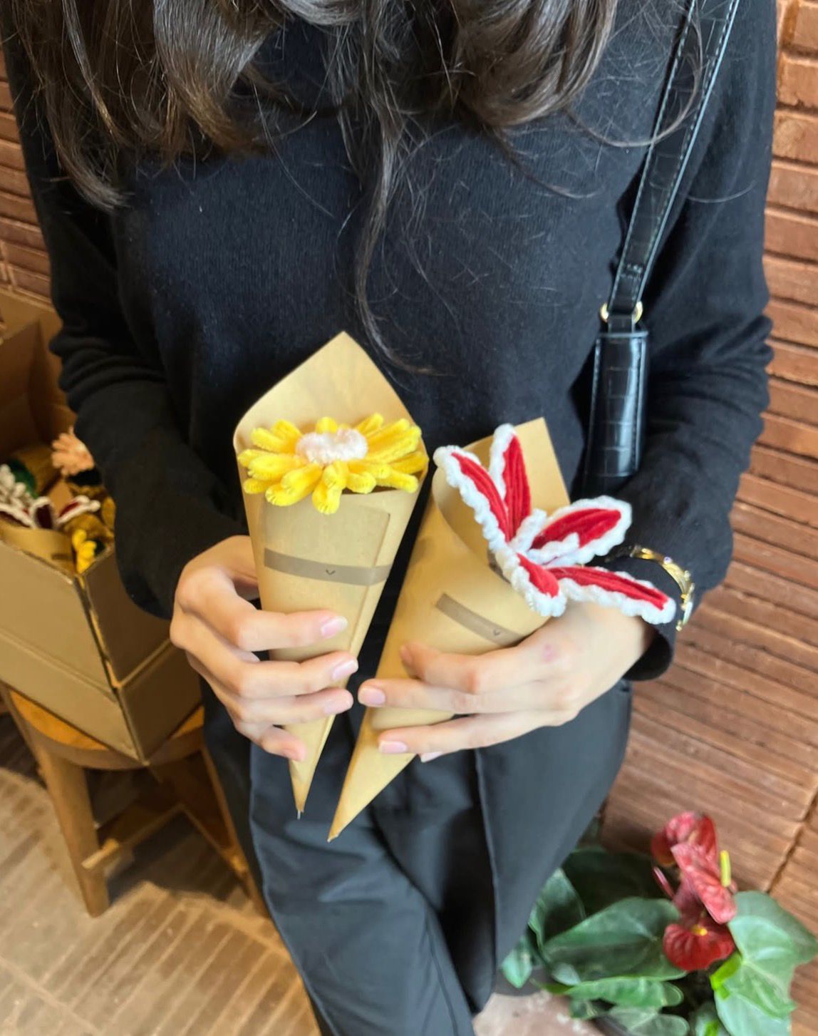 Person holding two paper cones with floral designs against a wooden wall.