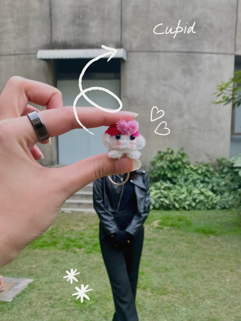 Small plush toy held by a hand with decorative elements, outdoors.