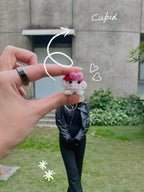 Small plush toy held by a hand with decorative elements, outdoors.