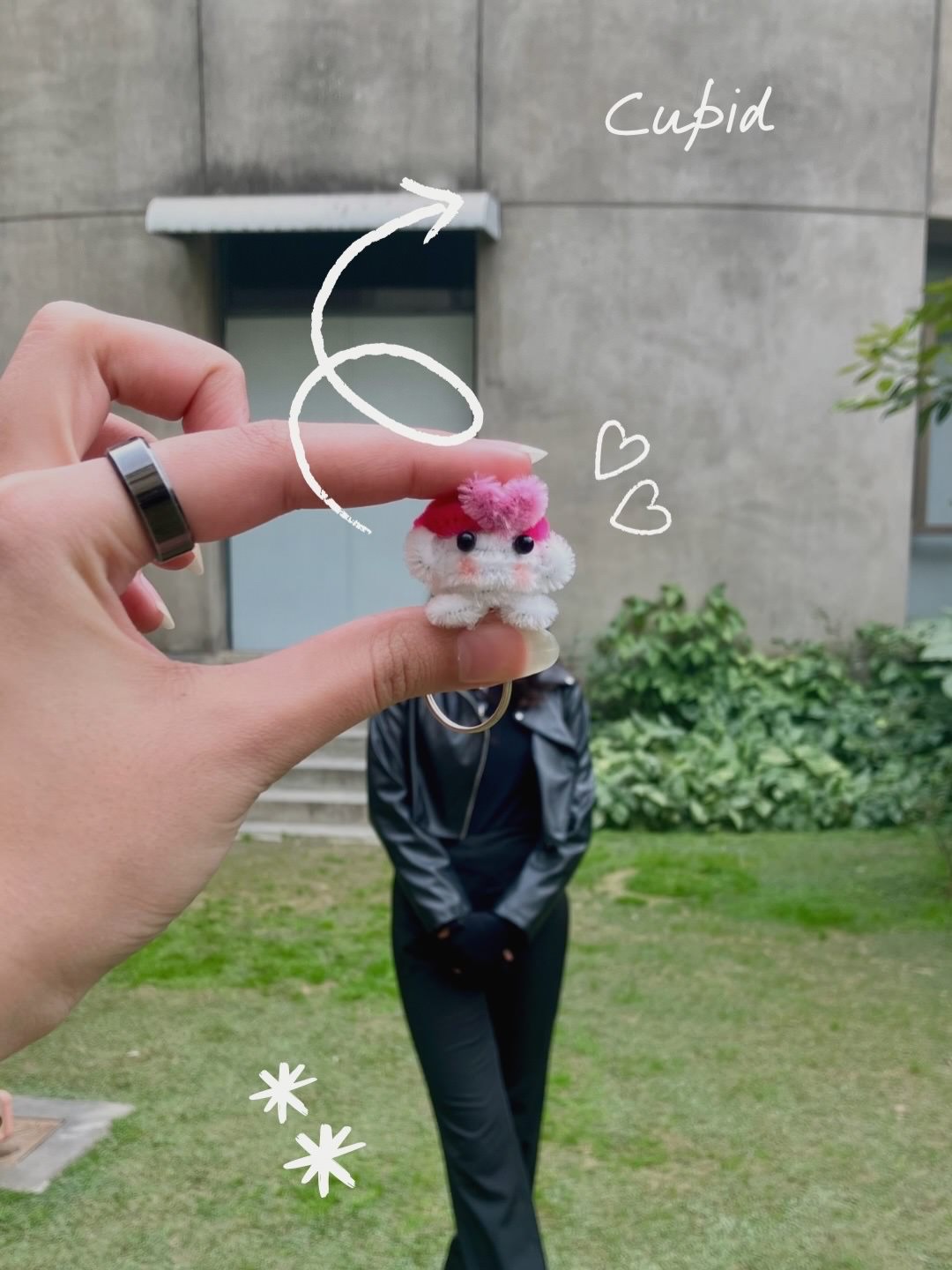 Small plush toy held by a hand with decorative elements, outdoors.