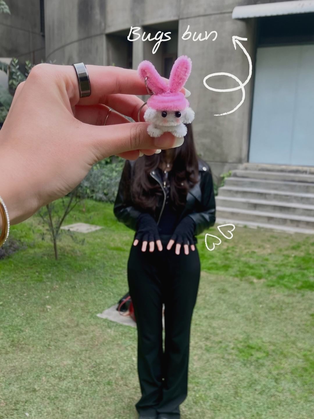 Person holding a small plush toy with a pink bunny head outdoors.