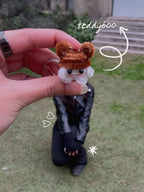 Small plush keychain held by a hand with decorative text overlay on a grassy background